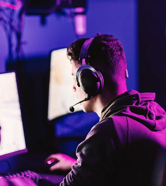 Vue de dos d'un joueur professionnel d'e-sport portant un casque pendant qu'il dispute une partie compétitive dans une salle de jeu sombre